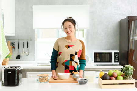 Young beautiful asian woman preparing yogurt and blueberry for breakfast in morning listen to musicの写真素材