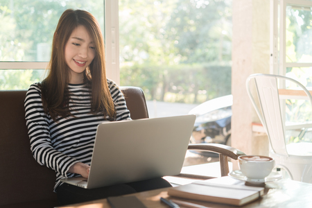 Beautiful young teenage woman freelance work with laptop at coffee shop in with sun light, freelance lifestyle conceptualの写真素材