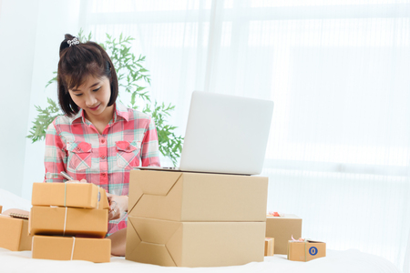 Woman small business owner, business start up in bedroom, young entrepreneur work with laptop prepare parcel boxes for deliver to customerの写真素材