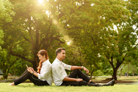 Man and woman in white shirt use smartphone without talk to each other in outdoors parkの写真素材
