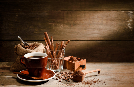A Cup of black coffee with coffee bean bag,cinnamon, and sugar on wooden floor with copyspace in backgroundの写真素材