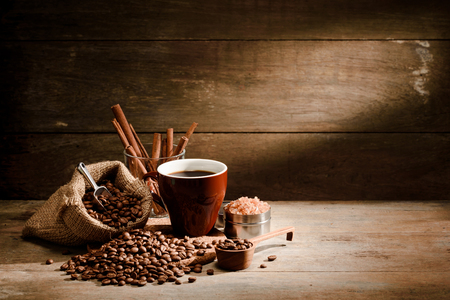 A Cup of black coffee with coffee bean bag,cinnamon, and sugar on wooden floor with copyspace in backgroundの写真素材