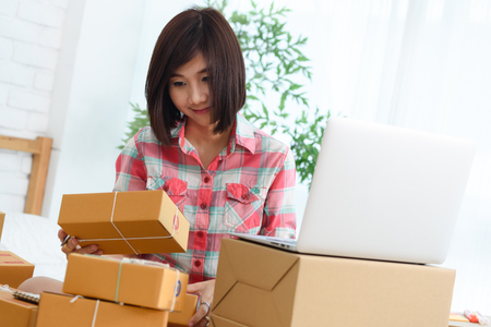 Woman small business owner, business start up in bedroom, young entrepreneur work with laptop prepare parcel boxes for deliver to customerの写真素材