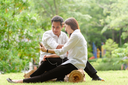 Man and woman in white shirt use smartphone together in outdoors parkの写真素材
