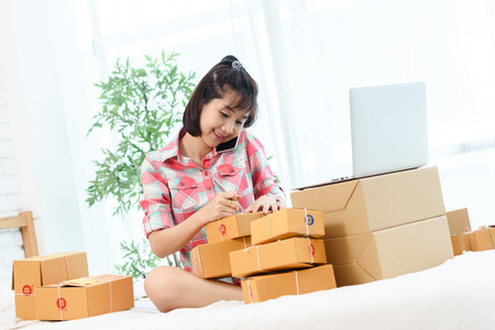 Woman small business owner, business start up in bedroom, young entrepreneur work with laptop prepare parcel boxes for deliver to customerの写真素材