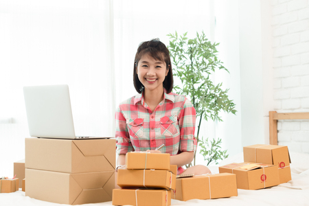 Woman small business owner, business start up in bedroom, young entrepreneur work with laptop prepare parcel boxes for deliver to customerの写真素材
