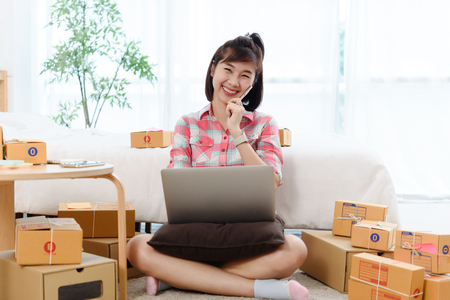 Happy Woman small business owner, business start up in bedroom, young entrepreneur work with laptop prepare parcel boxes for deliver to customerの写真素材