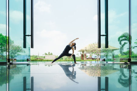 Young asian woman practicing yoga performing Revolved Side Angle Pose
with reflection on floorの写真素材