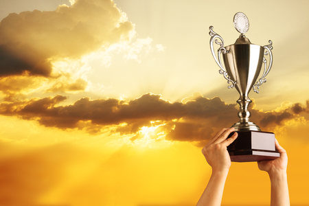Winning team raise trophy cup with background of sky of light rayの写真素材