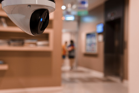 CCTV surveillance camera operating in front of elevator in buildingの写真素材