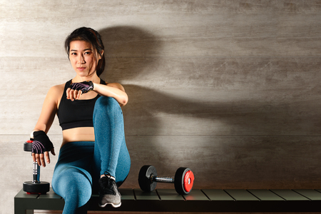 Young good looking woman rest while exercise with dumbells with copy space on wallの写真素材