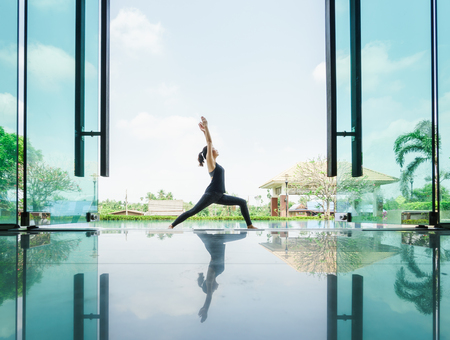 Young skinny asian woman practising yoga with reflection on tile floorの写真素材
