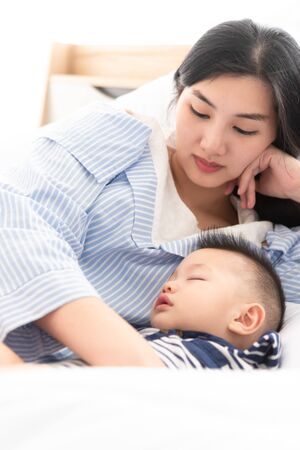 8 Months old baby sleep in bed with his mother in white bedroomの写真素材
