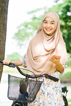 Portrait of smiling cute muslim girl use smartphone handle a bike, islamic teen lifestyleの写真素材