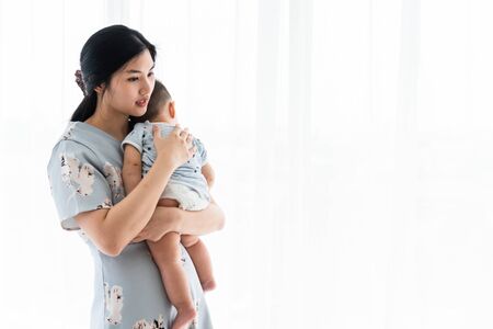 Mother soothe her son in white bed room by the windowの写真素材