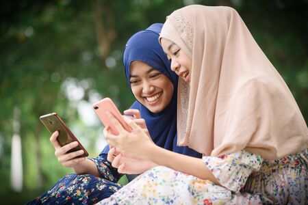 Two muslim woman use smartphone play social media together, two islamic girl wear hijab head scarfの写真素材