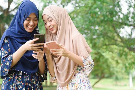 Two muslim woman use smartphone play social media together, two islamic girl wear hijab head scarfの写真素材