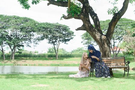 Two muslim teenage woman chill and relax in public park play social media on smartphone togetherの写真素材