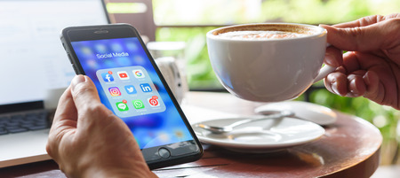 BANGKOK, THAILAND- 23th August 2019 : Hands of man use Iphone 7 plus with social media application icon of facebook, youtube, google search, instagram, twitter, linkedin, line whatsapp, and pinterest in a cafeのeditorial素材