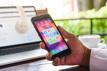BANGKOK, THAILAND- 23th August 2019 : Hands of an old man use Iphone 7 plus with social media application icon of facebook, youtube, google search, instagram, twitter, linkedin, line whatsapp, and pinterest in a cafeのeditorial素材