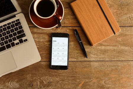 Screen of smartphone with calendar of year 2020 with laptop, pen and note book on coffee tableの写真素材