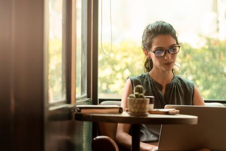 Beautiful caucasian woman wear glasses use internet via laptop in cafe during morningの写真素材