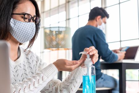 Woman wear mask use alcohol gel to clean her hands working at home during lock down period together with familyの写真素材
