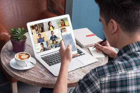 A man use laptop with screen of video conference meeting  with 9 other people and taking notes, work...