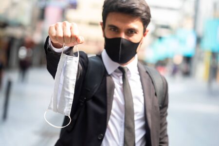 Businessman wearing black mask and show a white face mask encourage everyone to wear surgical mask, New normal of today's lifestyle with mask in everyday livesの写真素材