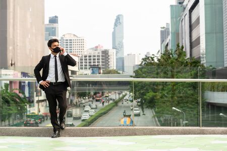 Businessman wearing suit and mask talking via smartphone make phone callの写真素材