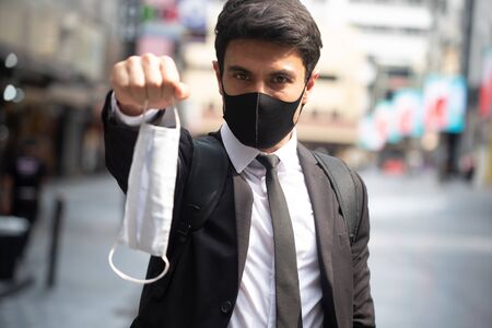 Businessman wearing black mask and show a white face mask encourage everyone to wear surgical mask, New normal of today's lifestyle with mask in everyday livesの写真素材