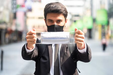 Businessman wearing black mask and show a white face mask encourage everyone to wear surgical mask, New normal of today's lifestyle with mask in everyday livesの写真素材