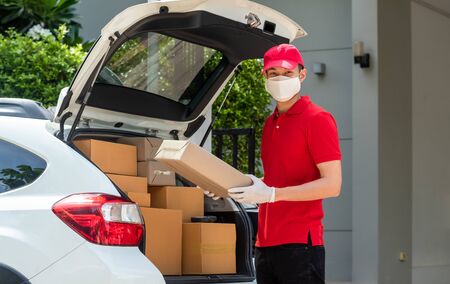 Delivery staff in red uniform delivering parcel to customer homeの写真素材