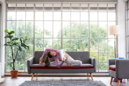 Young beautiful woman practicing yoga while reading magazine at homeの写真素材