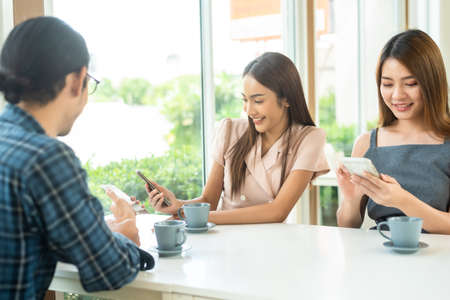 Three friends meet and see each other use smartphone play social media together in cafeの写真素材