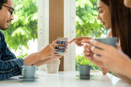 Three friends meet and see each other use smartphone play social media together in cafeの写真素材