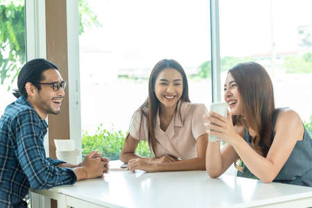 Three friends meet and see each other use smartphone play social media togetherの写真素材