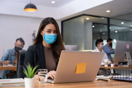 asian Woman business worker working with laptop wearing flu mask in office show new normal lifestyleの写真素材