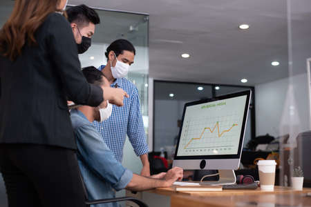 Four asian office worker analysing about kpi social media marketing result while everyone wearing mask as new normal lifestyleの写真素材