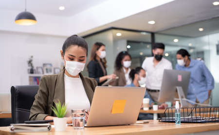 Woman business worker working with laptop wearing flu mask in office show new normal lifestyleの写真素材
