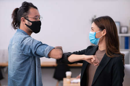 Two asian office worker make elbow bumb for greeting in stead of shaking handsの写真素材