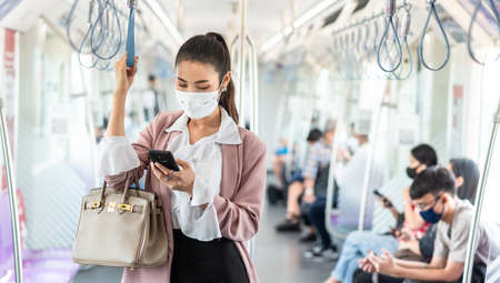 Asian business woman travelling on train in city wearing mask and pink blazerの写真素材