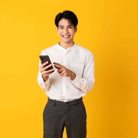 Young good looking asian man using smartphone isolated on yellow background pointing on screenの写真素材