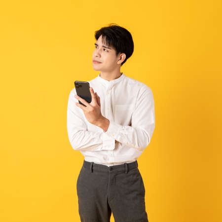 Young good looking asian man using smartphone isolated on yellow backgroundの写真素材