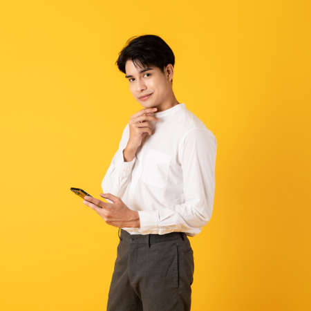 Young good looking asian man using smartphone isolated on yellow background surprisingの写真素材