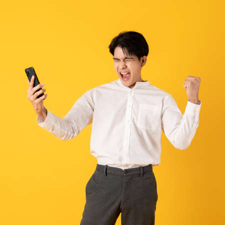 Young good looking asian man using smartphone isolated on yellow background surprisingの写真素材