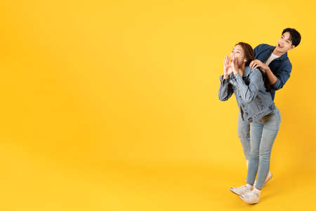 Two Young good looking asian couple using isolated on yellow background shouting at space area...
