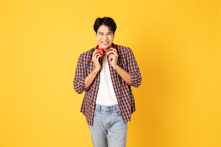 Smile happy asian man wearing scottish shirt with jeans isolated on yellow background using smartphone and headphone and laughingの写真素材