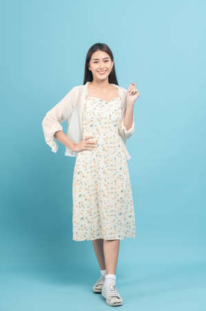 Beautiful young asian woman in white dress with flower pattern isolated on blue backgroundの写真素材