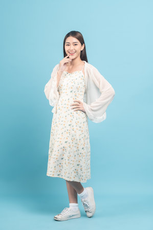 Beautiful young asian woman in white dress with flower pattern isolated on blue backgroundの写真素材